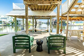 A wooden deck with a hammock, green chairs, and a table by a water body. - Anchor Down - Bay & Beach Spot, Fire Pit, Boat Slip! (Galveston)
