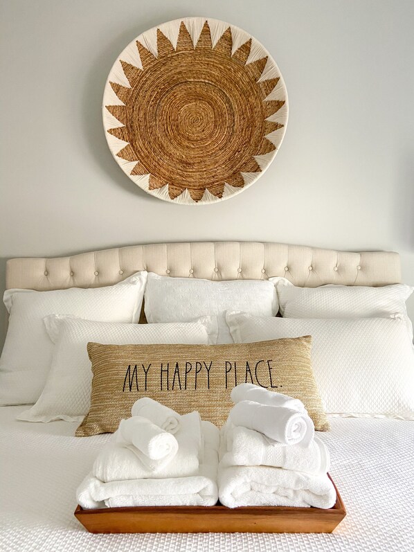 A neatly made bed with white linens, a woven wall hanging above, and a pillow with "MY HAPPY PLACE" embroidered on it. - NEW & Modern South Haven Beach House (South Haven)