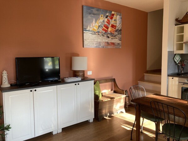 A living room with a TV, a painting, a dining table, and a kitchen area.