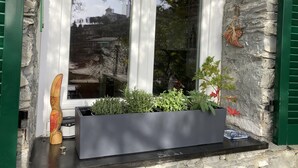 Eine Steinsäule mit einem Fenster, ein Pflanzkasten mit Pflanzen und eine Holzskulptur.