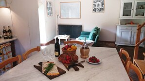A dining area with a marble table, wine bottle, glasses, and a basket of fruit.