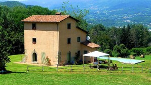 A two-story building with a tiled roof, a small porch, and a swimming pool in the background.