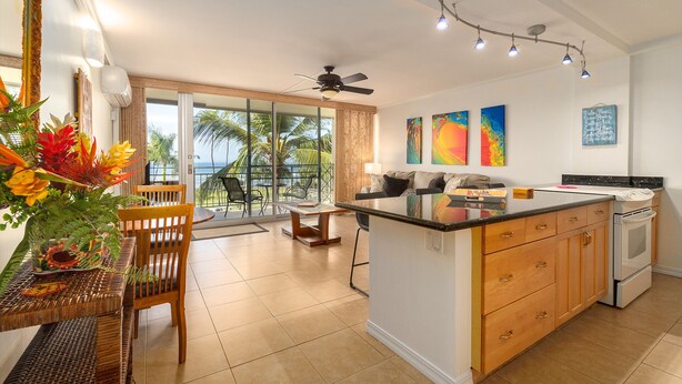 A spacious kitchen with a central island, a dining area with a view of the ocean, and a living area with artwork and a ceiling fan. - Island Surf Resort, breathtaking ocean view, in the heart of the action (Kihei)