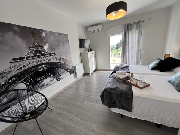 Un dormitorio con un gran mural de la Torre Eiffel, una cama, una silla y un aparador.