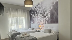 A hotel room with two beds, a large floral wall mural, a ceiling light, and a window with sheer curtains. - Rural House Altaret (Callosa d'en Sarrià)