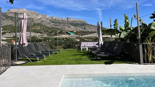 A pool area with lounge chairs and umbrellas, a grassy lawn, and a mountainous backdrop. - Rural House Altaret (Callosa d'en Sarrià)