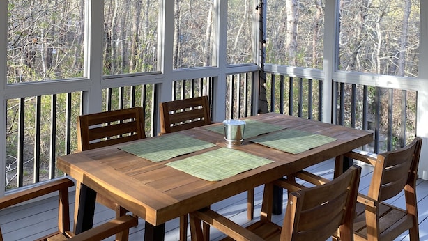 A wooden deck with a table and chairs, surrounded by large windows with a view of trees. - Wellfleet Woodlands Escape - Privacy in the Pines! (Wellfleet)