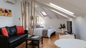 Un dormitorio tipo loft moderno con techo inclinado, una cama grande, un escritorio y un televisor.