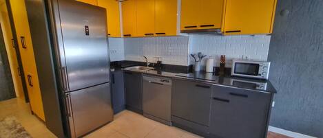 A modern kitchen with stainless steel appliances, yellow cabinets, and a tiled backsplash.