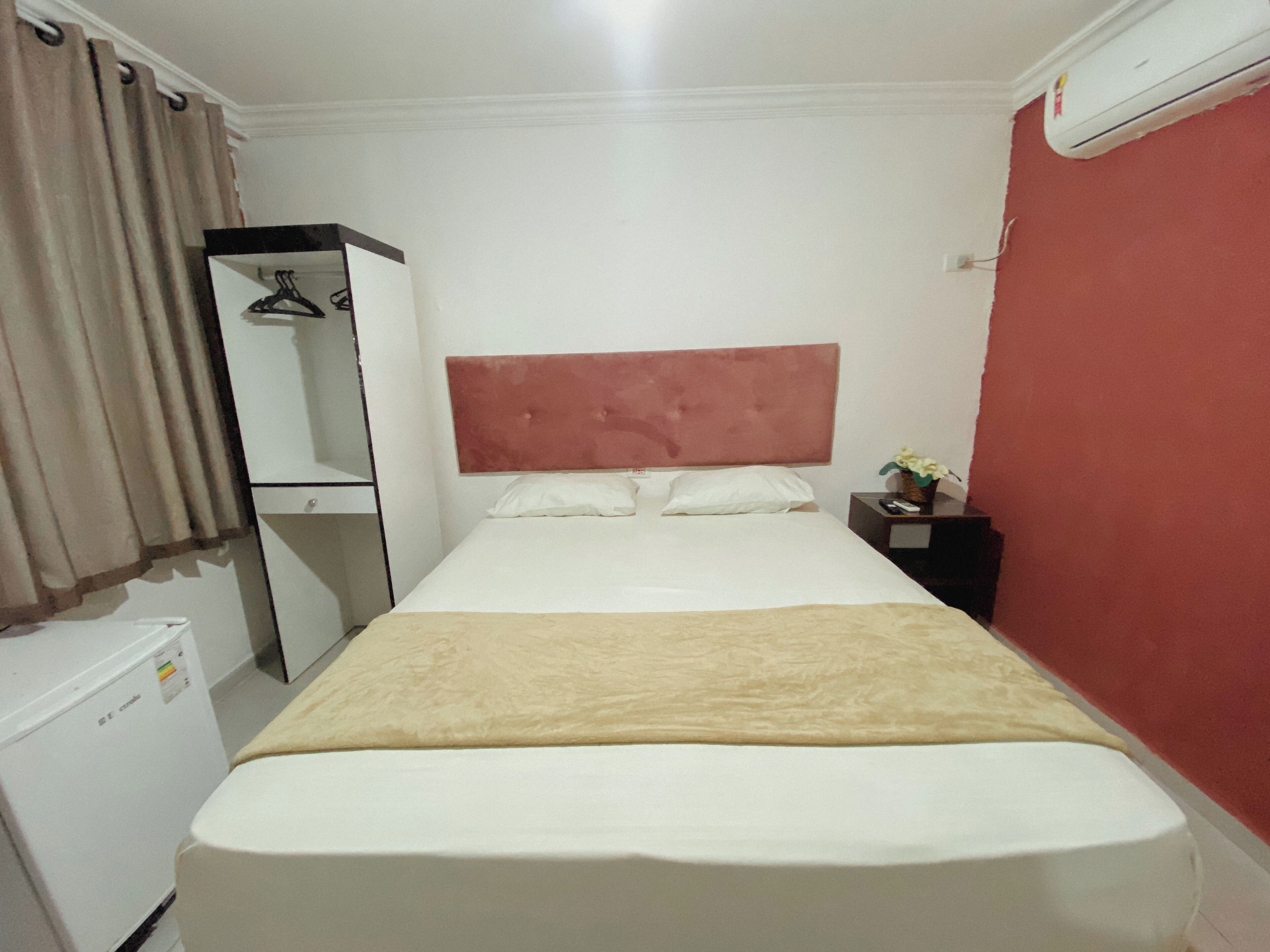 Een hotelkamer met een bed, een kledingkast, een kleine tafel met een vaas en een airconditioner.