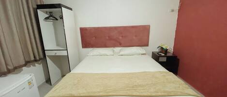 Een hotelkamer met een bed, een kledingkast, een kleine tafel met een vaas en een airconditioner.