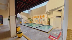 An outdoor swimming pool area with tiled flooring, potted plants, and a covered seating area. - Hotel 5 Sóis (Olinda)