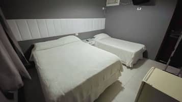 A hotel room with two beds, a flat-screen TV mounted on the wall, and a small kitchenette.