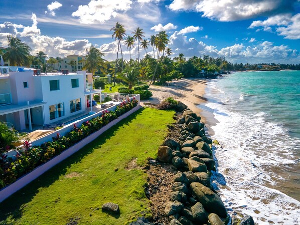 A beachfront property with a modern white building, a grassy lawn, and a rocky shoreline. - Large Ocean Front Home on Sandy Beach With Pool (Medianía Alta)