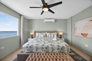A bedroom with a bed, a ceiling fan, a window with a view of the sea, and a wall-mounted air conditioner. - Large Ocean Front Home on Sandy Beach With Pool (Medianía Alta)