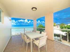 A balcony with a white table and chairs, overlooking a beach and ocean. - Large Ocean Front Home on Sandy Beach With Pool (Medianía Alta)