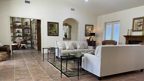A spacious living room with a sofa, coffee table, and a fireplace. There is a bookshelf and a door leading to another room. - Casa Blanca Main House, Riverview, 10 Beds, Group-Friendly (Kerr County)