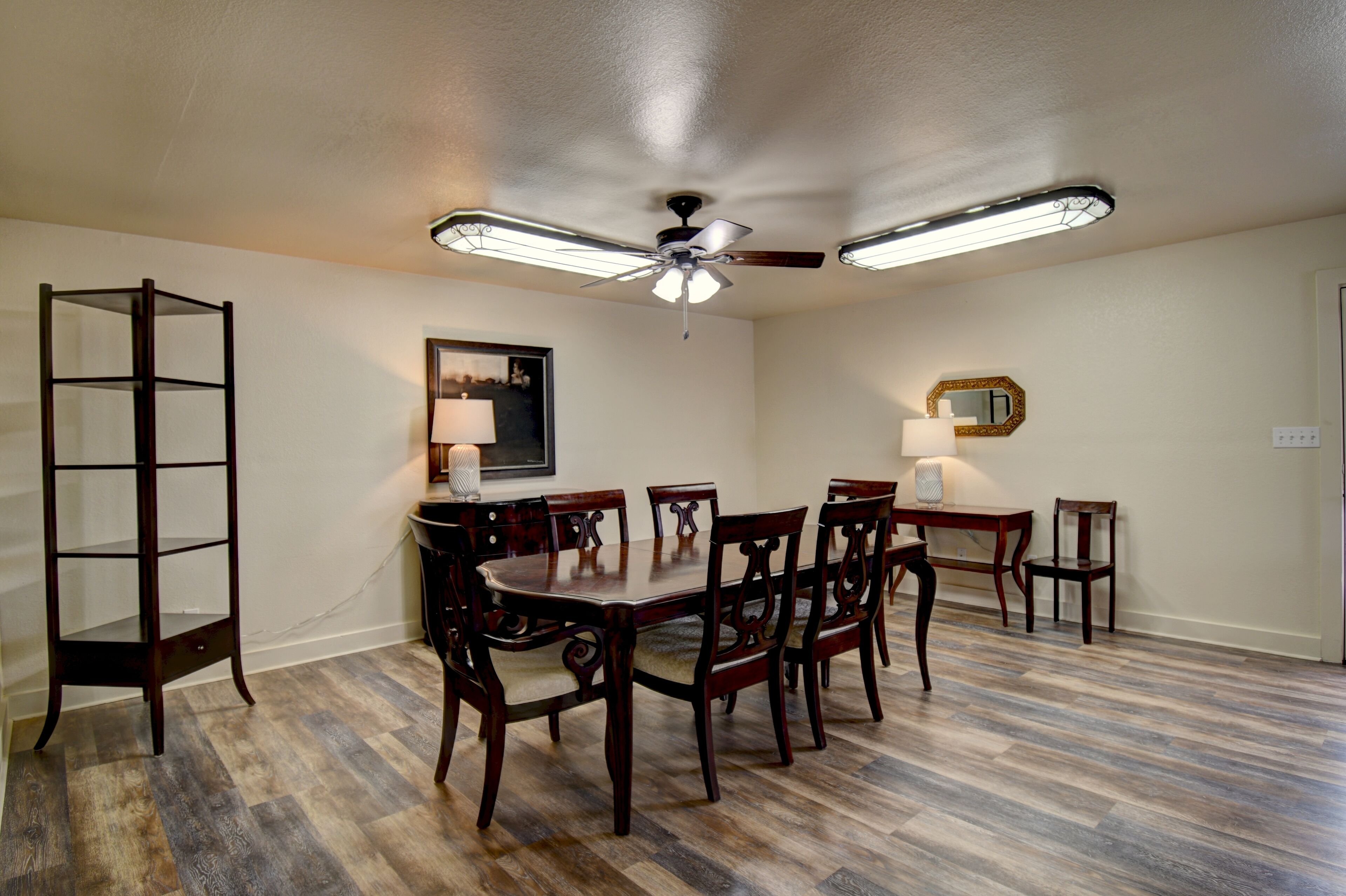 Une salle à manger avec une table et des chaises en bois, un ventilateur de plafond et un lustre.