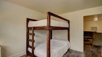 A bunk bed with wooden railings and white bedding in a room with wooden flooring and a door leading to another room.