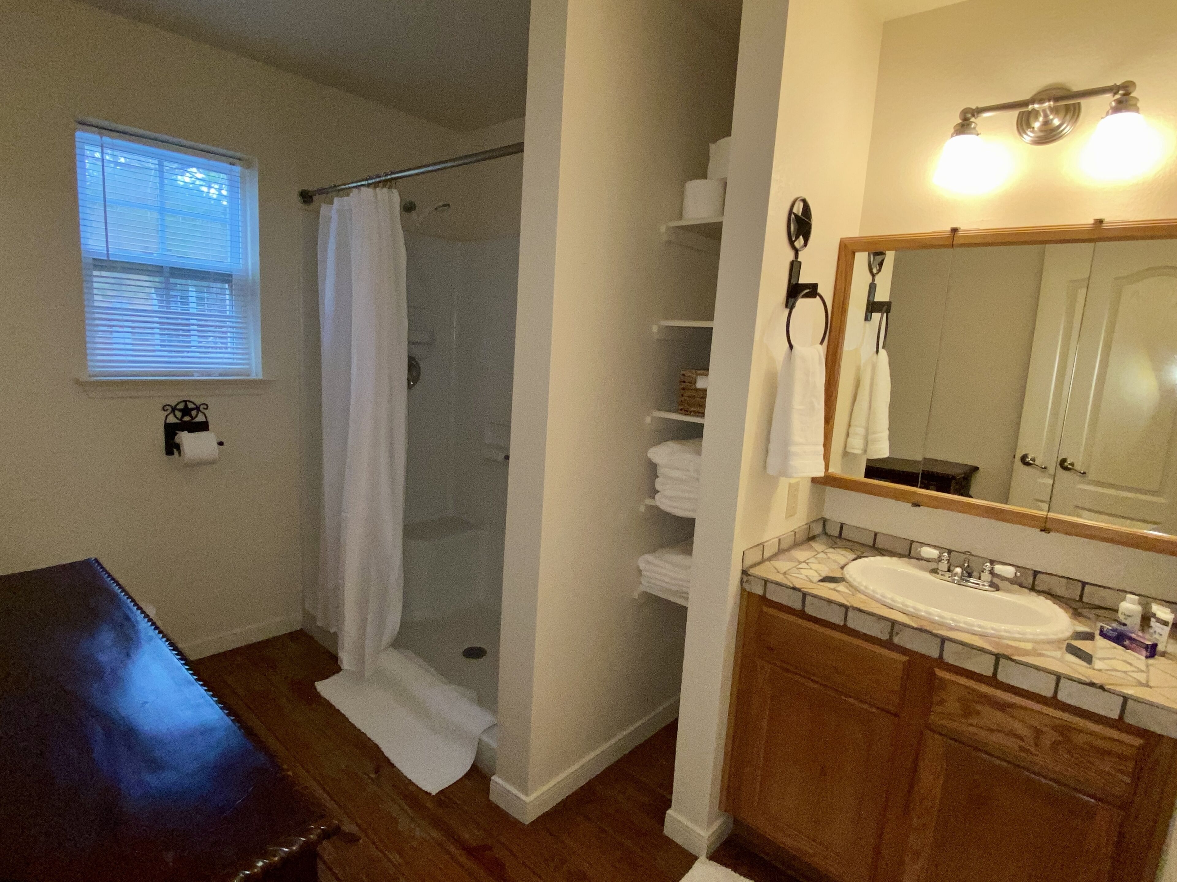 A bathroom with a wooden vanity, a sink, a mirror, a shower with a curtain, and a toilet paper holder on the wall.