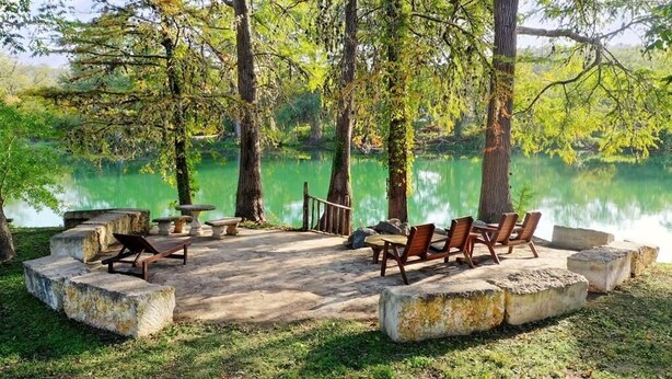 An outdoor seating area with stone tables and chairs, surrounded by trees and a lake. - Cabin A at Casa Blanca, 1BR/1BA, Sleeps 4, Porch, Grill (Ingram)