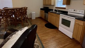 A kitchen with wooden cabinets, a stove, a sink, and a dining area with a table and chairs. - Cabin A at Casa Blanca, 1BR/1BA, Sleeps 4, Porch, Grill (Ingram)