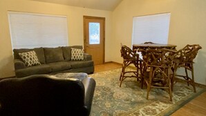A living room with a sofa, a dining table with chairs, a ceiling fan, and a door with a window. - Cabin A at Casa Blanca, 1BR/1BA, Sleeps 4, Porch, Grill (Ingram)