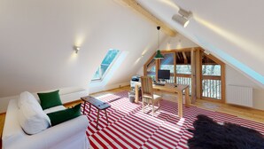 A cozy loft bedroom with a sloped ceiling, a wooden desk with a computer, a chair, and a large window offering a view of trees. - Charming guest apartment in an old farmhouse in a secluded alpine location (Sonnberg)
