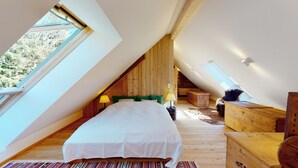 A bedroom with a sloped ceiling, wooden walls, a bed with white bedding, a lamp, and a rustic wooden chest. - Charming guest apartment in an old farmhouse in a secluded alpine location (Sonnberg)