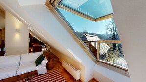 A cozy attic bedroom with a skylight, wooden beams, a white sofa, and a view of the surrounding landscape. - Charming guest apartment in an old farmhouse in a secluded alpine location (Sonnberg)