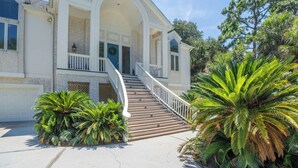 Une maison à deux étages avec un escalier central, un garage et des plantes tropicales.