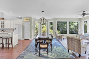 A spacious kitchen with white cabinets, a dining area with a large table, and a view of lush greenery through large windows. - Tabby on the Tee - Four Bedroom House, Sleeps 15 (Fripp Island)