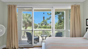 Une chambre avec un grand lit, un ventilateur et une vue sur un balcon équipé de chaises et d’une table.