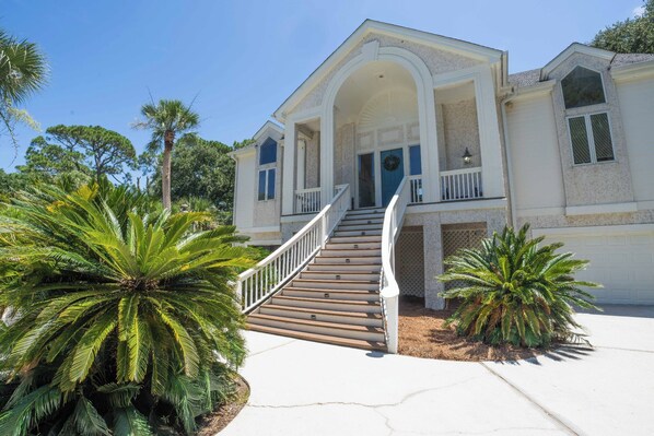A two-story house with a central staircase, large windows, and a front porch. - Tabby on the Tee - Four Bedroom House, Sleeps 15 (Fripp Island)