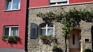 A stone building with a red facade, a wooden door, and two windows with shutters. - Weingut Manuel Sauer (Nordheim a. Main)