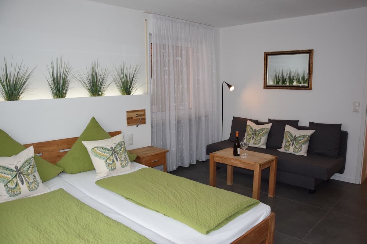 A bedroom with a bed, a sofa, a small table, and a lamp.