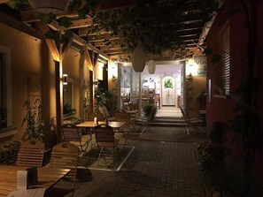 An outdoor café area with wooden tables and chairs, surrounded by plants and a brick pathway. - Weingut Manuel Sauer (Nordheim a. Main)