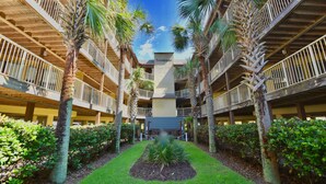 A courtyard with a central garden, surrounded by multi-level balconies with railings, and palm trees. - Popular property on the beach with family atmosphere (Gulf Shores)