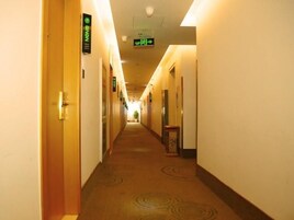 Pasillo de hotel con puertas a ambos lados, suelo alfombrado y un cartel que indica la dirección al ascensor.