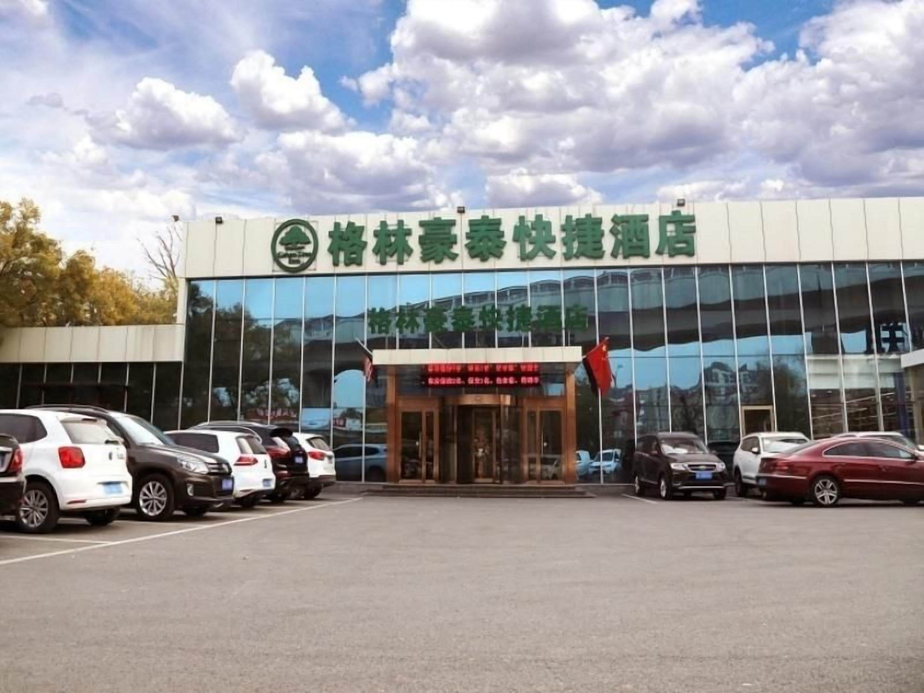 Hotel com fachada moderna, estacionamento com vários carros e céu claro.