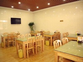 Un salón de conferencias con varias mesas y sillas, un televisor de pantalla plana montado en la pared y una planta en maceta.