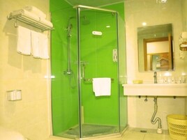Un baño con ducha de vidrio, lavamanos con espejo y toallero con toallas.
