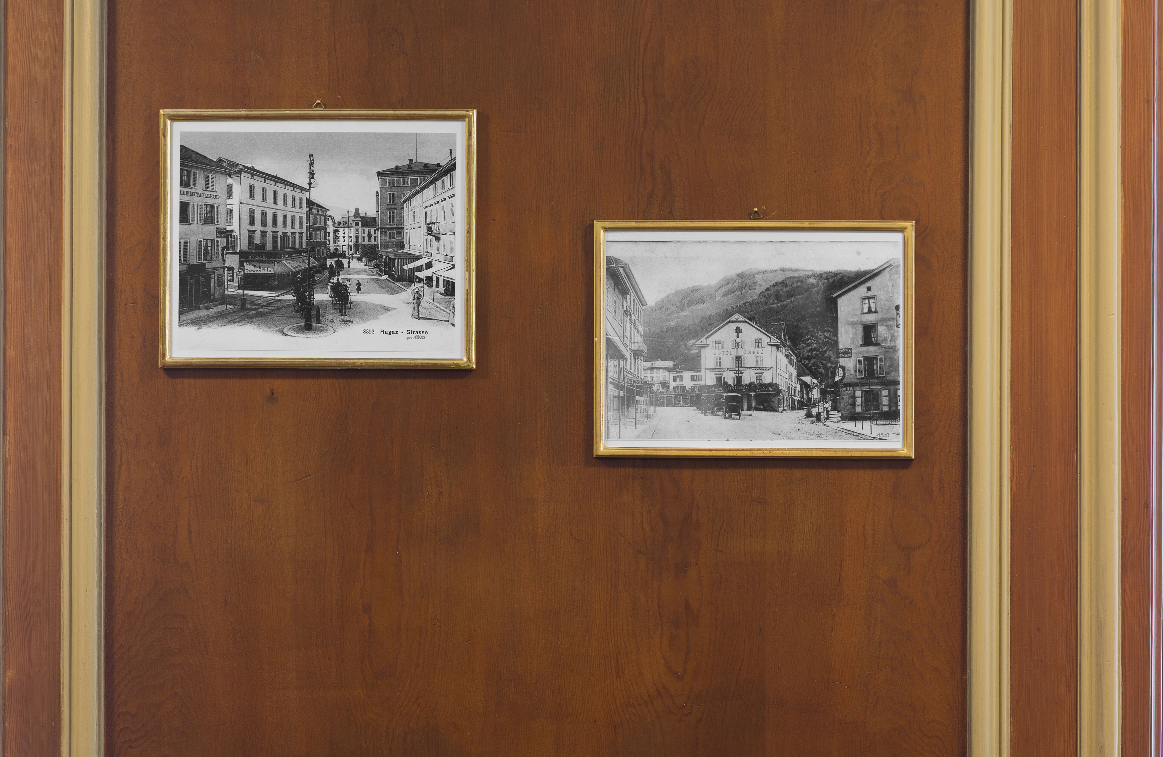 Dues fotografies en blanc i negre, emmarcades, que mostren escenes urbanes penjades d'una paret de fusta.