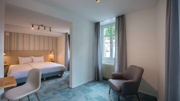 A hotel room with a bed, a chair, a table, and a window with curtains.