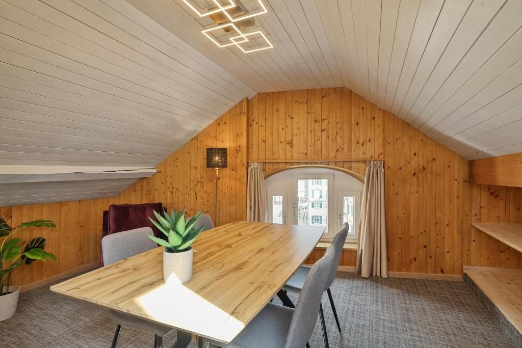 Una habitación con techo de madera, una mesa de comedor de madera, una planta en maceta y vistas al exterior por una ventana.