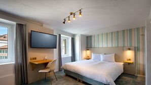 Habitación de hotel con cama, escritorio, silla, televisor y ventana con cortinas.