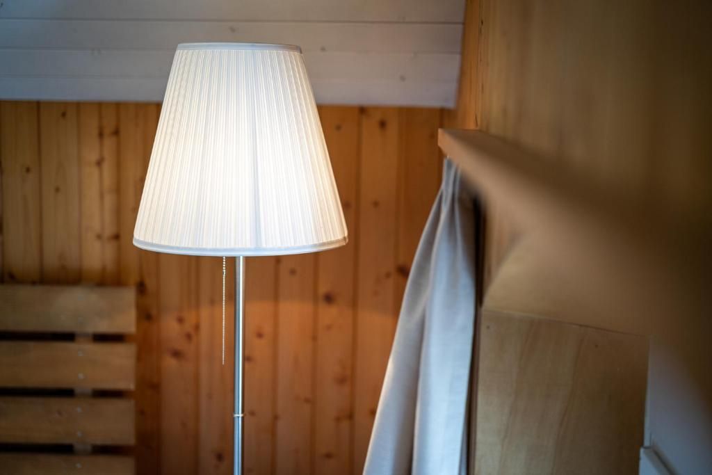 Una habitación con una lámpara sobre un piso de madera, una pared de madera y una cortina.