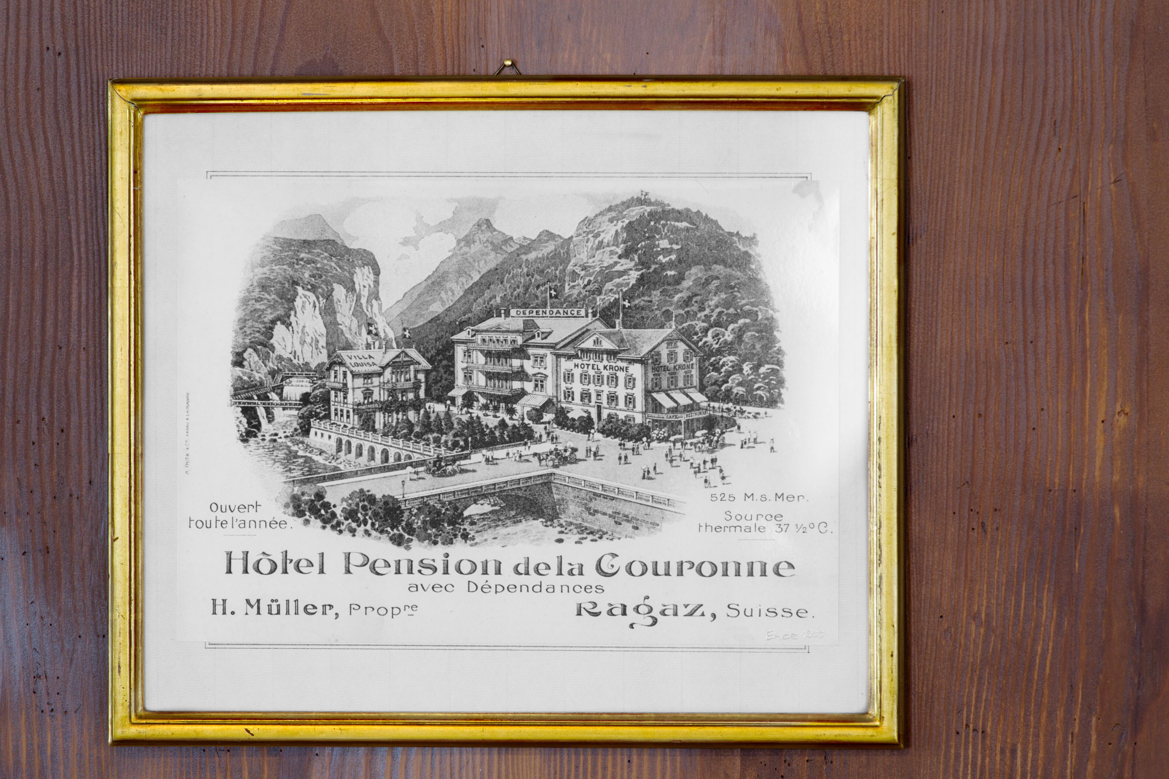 A black and white illustration of Hotel Pension de Couronne in Ragaz, Switzerland, featuring a mountain backdrop and a bridge.