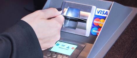 A hand inserting a card into a payment terminal with Visa and MasterCard logos.