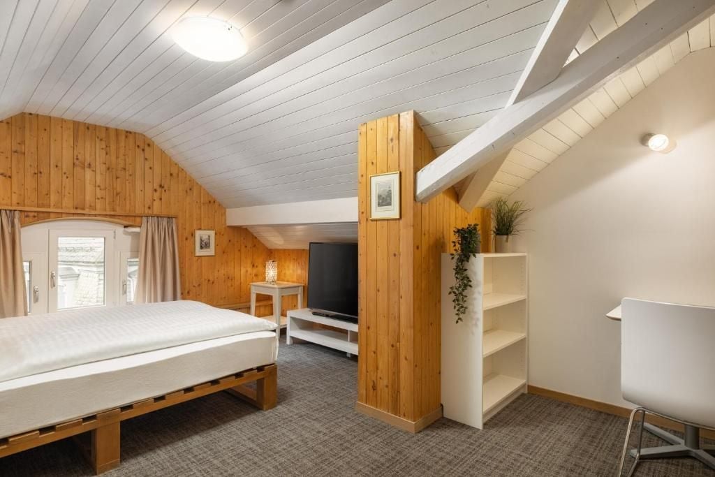 Een slaapkamer met een bed, een televisie, een klein tafeltje en een plank.